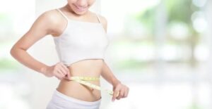 A woman is measuring her waist with a tape measure.