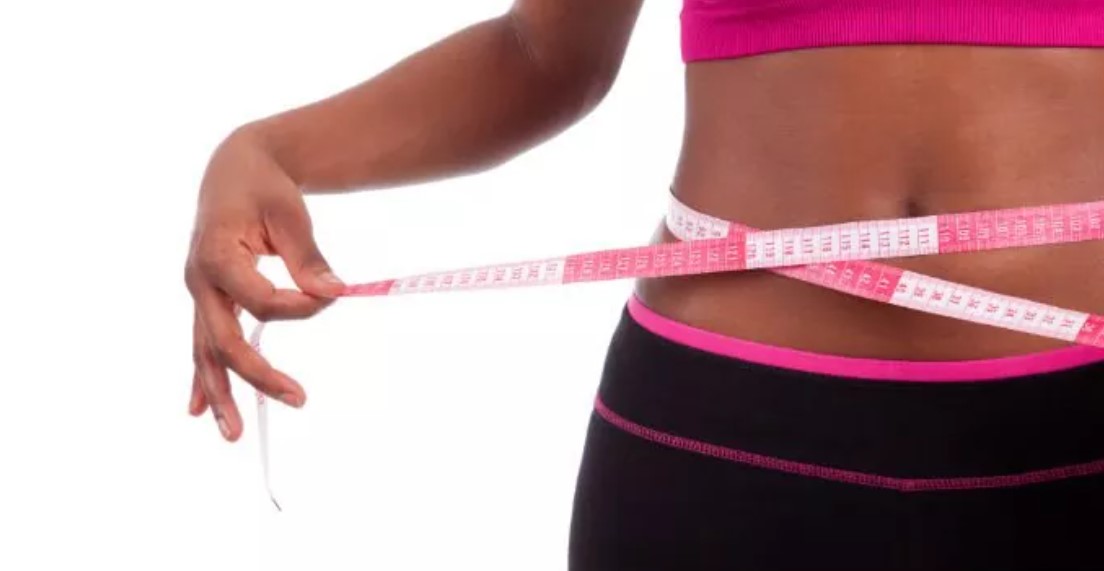 A woman is measuring her waist with a tape measure.