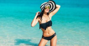 A woman in black bikini and hat on the beach.