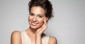 A woman with brown hair and a white shirt is smiling.