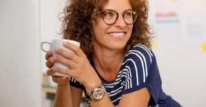 A woman with curly hair and glasses holding a cup.