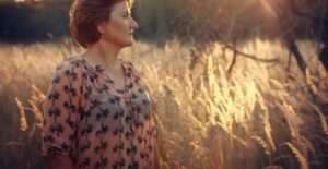 A woman standing in the grass looking off into the distance.