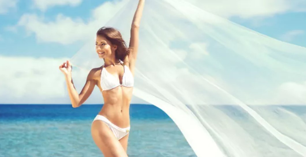 A woman in white bikini standing on the beach.