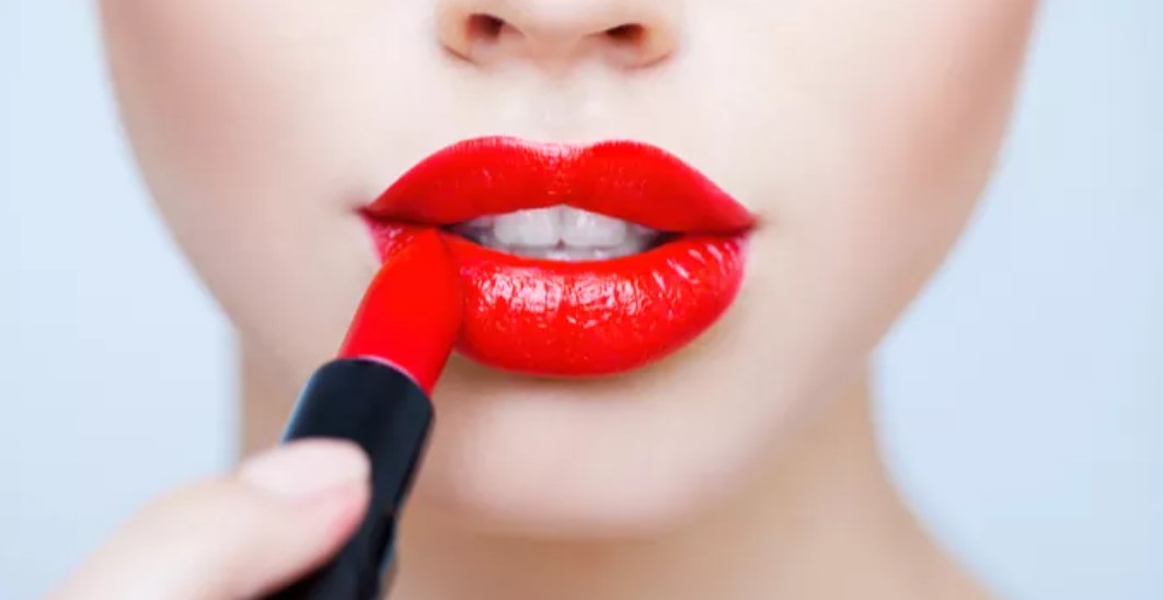 A woman is putting lipstick on her lips.
