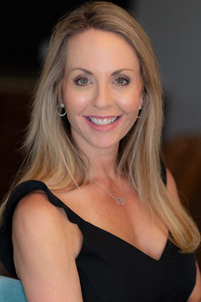 Smiling woman with long blonde hair in black dress.